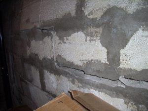 Bowing and cracking cinder block wall with visible old patchwork repairs, illustrating potential structural issues in a basement setting.
