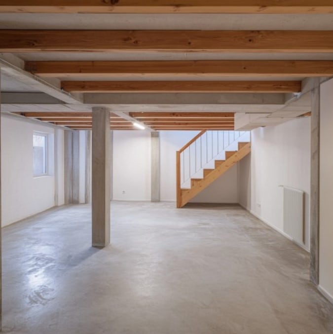 Empty basement interior with exposed wooden beams, concrete columns, and a staircase, illustrating a space ready for waterproofing and moisture control solutions.