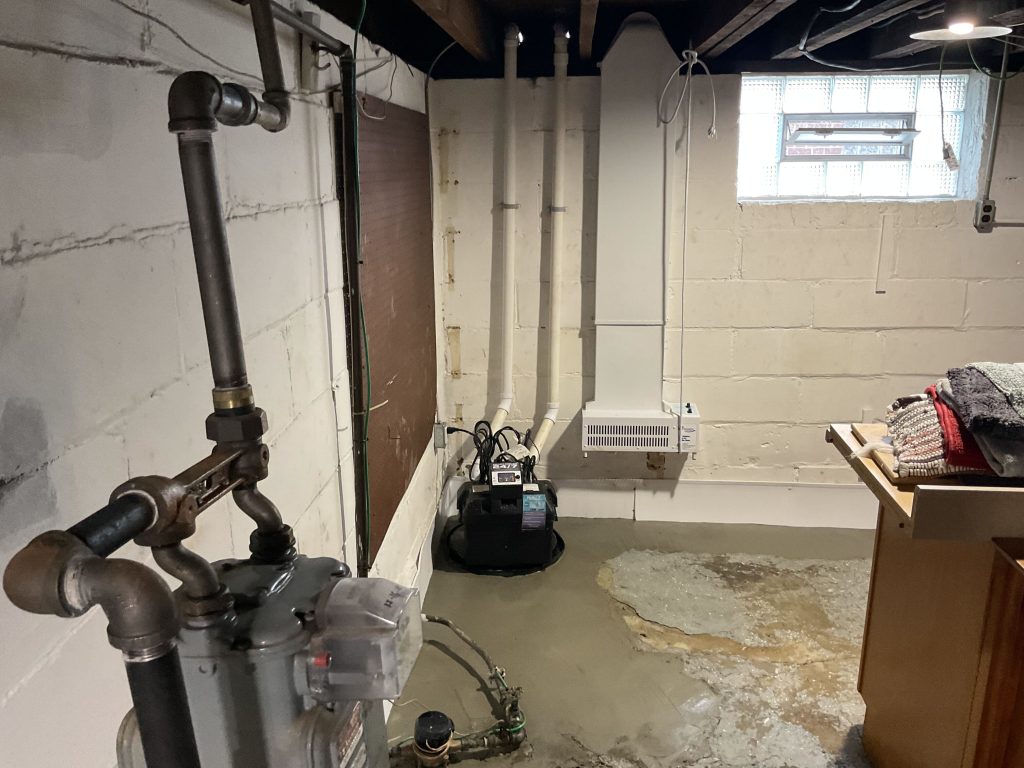 Sump pump installation in a basement with visible water accumulation, highlighting the importance of waterproofing solutions to prevent flooding and water damage.