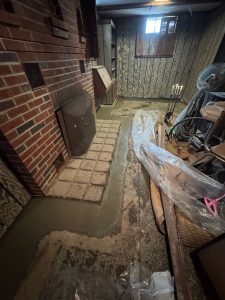 Basement undergoing waterproofing with freshly applied concrete, cluttered with tools and materials, illustrating repair efforts to prevent water leakage after heavy rain.