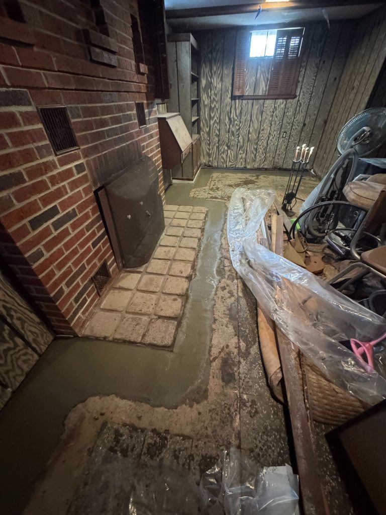Flooded basement with standing water on the floor, brick wall, and cluttered surroundings, illustrating water leakage issues commonly addressed by waterproofing solutions.