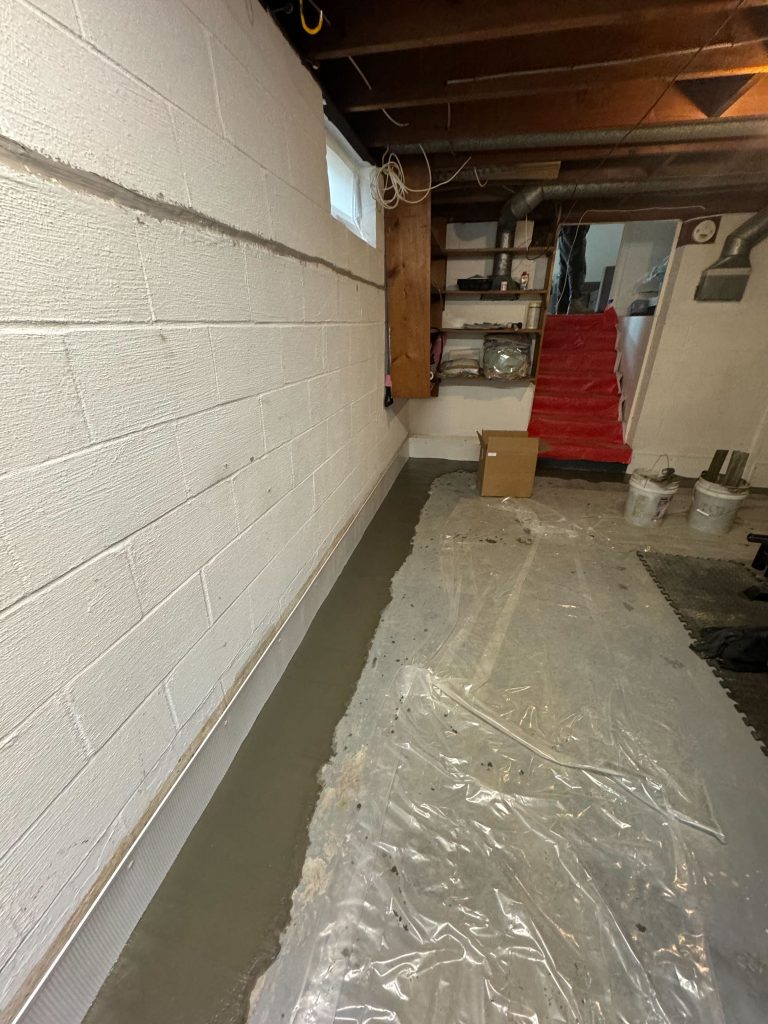 Basement waterproofing process with freshly applied concrete along the wall, showcasing a clean, prepared space for moisture prevention.