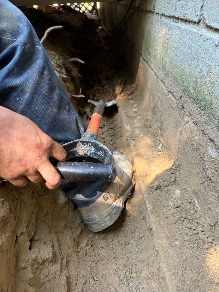 Person using a shovel to excavate soil near a foundation wall, demonstrating basement waterproofing techniques for moisture prevention in Ohio homes.
