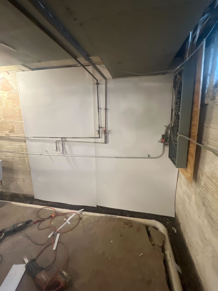 Basement wall with moisture barrier installation, visible plumbing and electrical components, illustrating waterproofing efforts to protect against water damage.