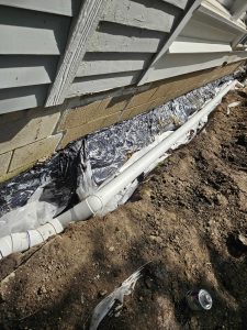Waterproofing system installation featuring drainage pipes and protective sheeting along the foundation of a home, illustrating prevention measures against water intrusion.