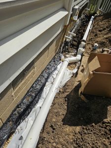 A newly installed drainage system alongside a house, featuring white PVC pipes and black tarp over gravel, conveying a sense of careful construction.