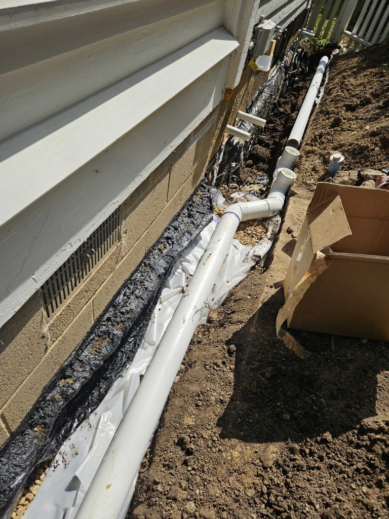 French drain installation with perforated pipe, gravel, and drainage fabric along a home's foundation, showcasing waterproofing measures to prevent basement flooding.