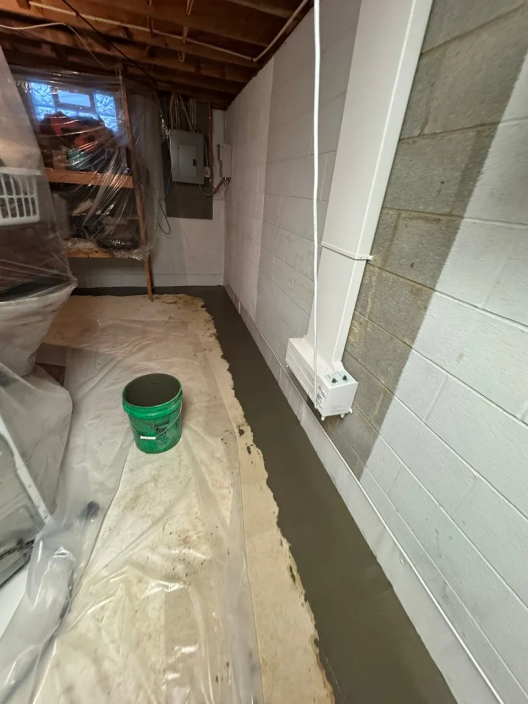 Completed basement waterproofing project in Kent, OH featuring an interior drain tile system, fresh concrete restoration, and EZ Breathe ventilation unit for moisture control.